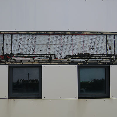 Grey building with a large section of damaged siding that is under repair Grey building with a large section of damaged siding that is under repair