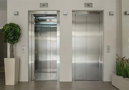 Photo of two silver elevators in a condo surrounded by potted plants Photo of two silver elevators in a condo surrounded by potted plants