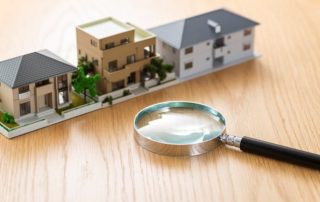 A magnifying glass sits next to miniature houses and condos on a wooden desk