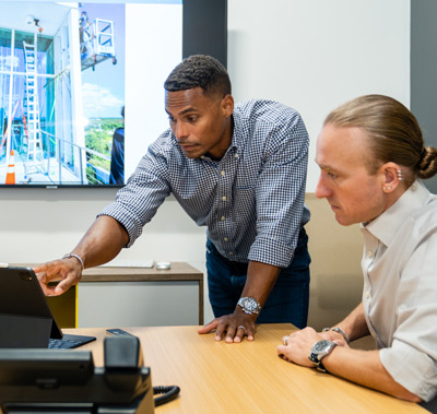 Scott works with team member to analyze a building floor plan on an ipad at the Building Mavens office.