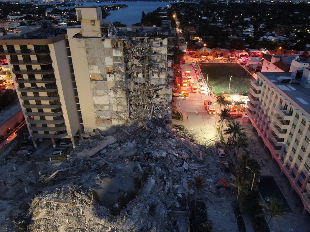 Aerial view of the Surfside condominum collapse at night with firetrucks nearby.