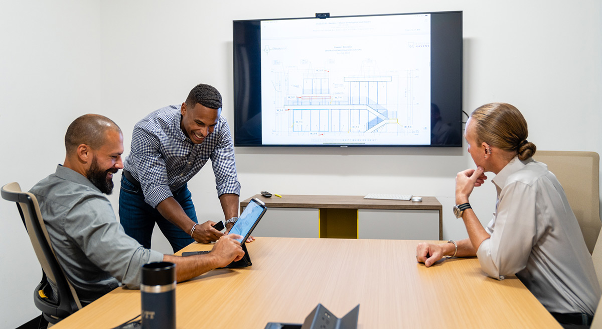 Building Mavens team smiles while studying building plans in an office meeting.