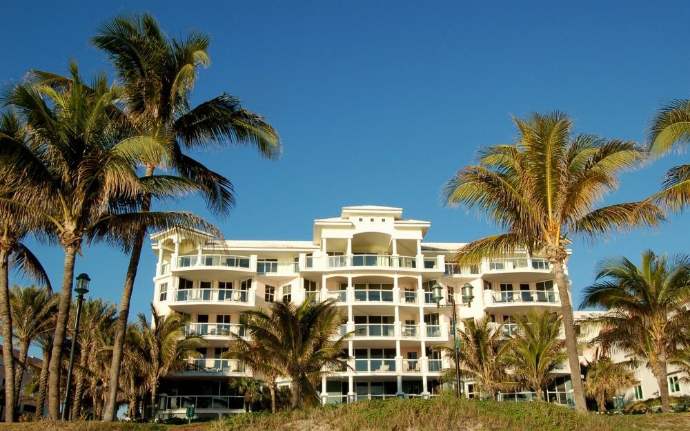Luxury beachfront condominium with expansive balconies, palm-lined frontage, and oceanfront views in an upscale Florida coastal community.