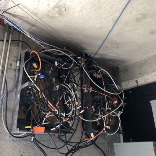 Overloaded electrical panel with tangled wiring found during building inspection.
